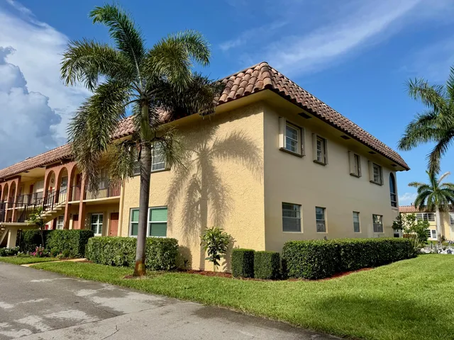 a view of a white house with a large windows and a yard with plants and large trees