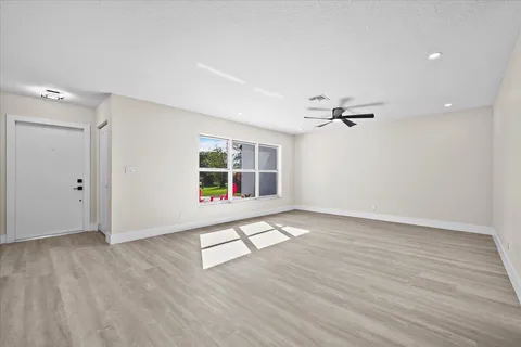 an empty room with wooden floor a ceiling fan and windows