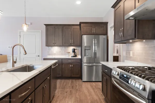 a kitchen with stainless steel appliances granite countertop a stove a sink dishwasher a refrigerator and wooden cabinets with wooden floor