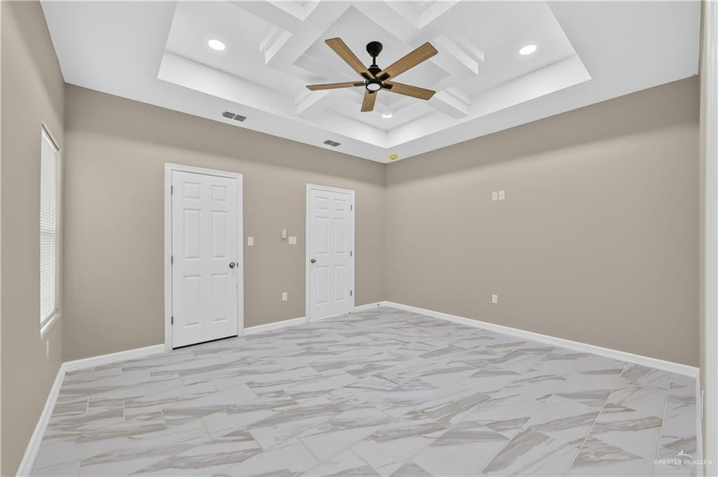 1920 Trinity Street Donna, TX 78537 - Photo 16 of 23 Spacious room featuring a tiered tray ceiling with recessed lighting and a ceiling fan, light-toned wall paint, two paneled doors, and large format tile flooring