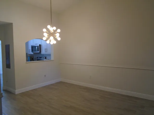 an empty room with a chandelier fan and wooden floor