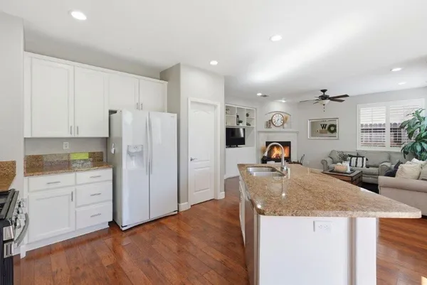 a living room with stainless steel appliances kitchen island granite countertop a refrigerator a sink a stove and white cabinets with wooden floor