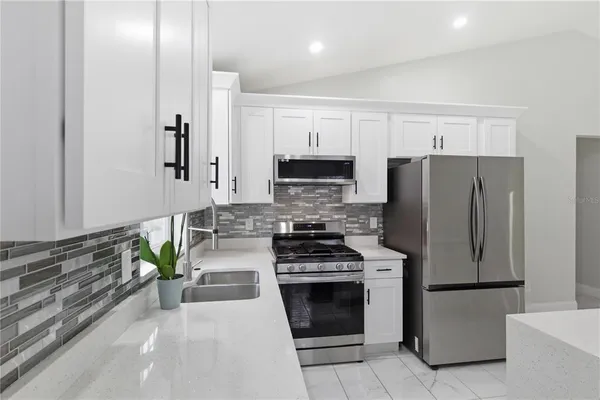 a kitchen with stainless steel appliances a refrigerator a stove a sink and white cabinets