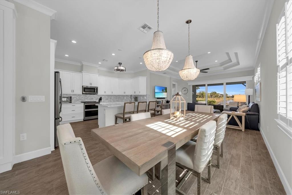 5756 Elbow Avenue Naples, FL 34113 - Photo 11 of 45 Dining area featuring ornamental molding, a chandelier, dark wood-style flooring, a raised ceiling, and ceiling fan