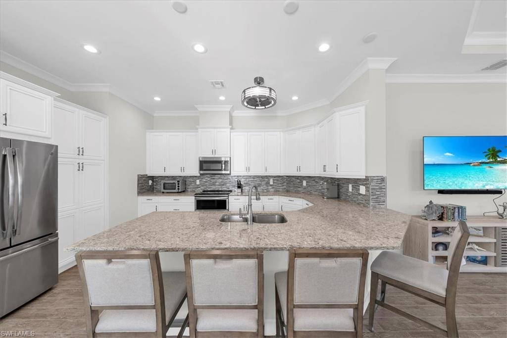 5756 Elbow Avenue Naples, FL 34113 - Photo 13 of 45 Kitchen featuring stainless steel appliances, backsplash, a breakfast bar area, ornamental molding, and white cabinets