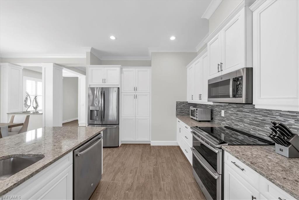 5756 Elbow Avenue Naples, FL 34113 - Photo 45 of 45 Kitchen with appliances with stainless steel finishes, crown molding, white cabinetry, light stone counters, and open floor plan