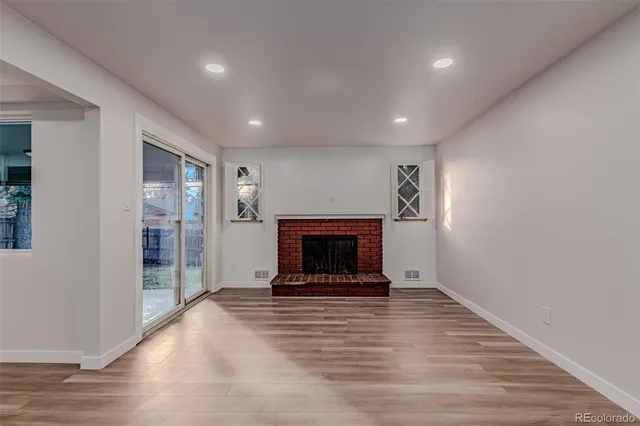 an empty room with wooden floor fireplace and windows