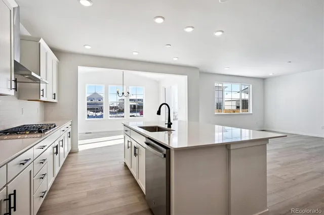 a large kitchen with stainless steel appliances granite countertop a stove a sink dishwasher and white cabinets with wooden floor