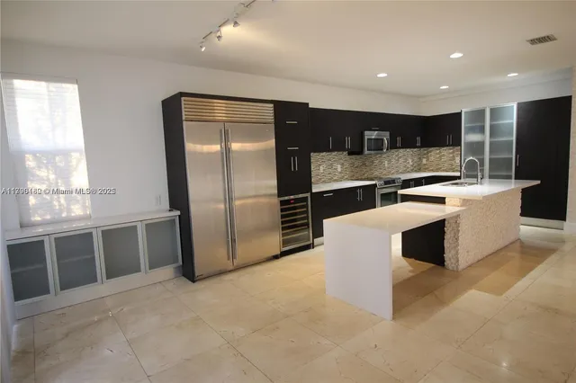a large kitchen with kitchen island a large counter top stainless steel appliances and cabinets