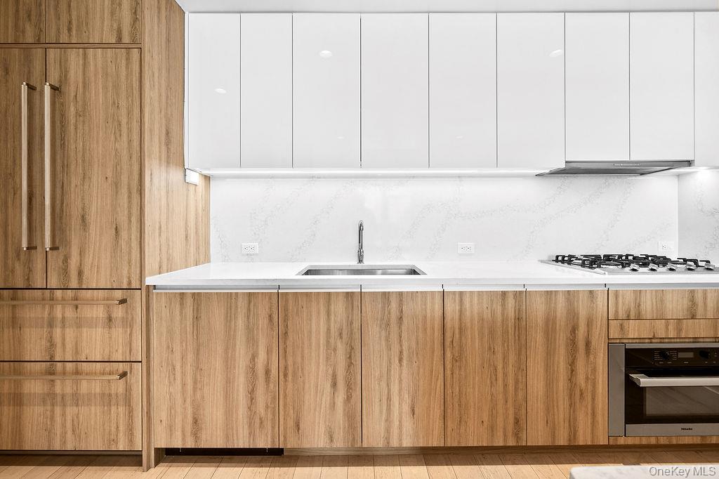 136-18 Maple Avenue, Unit 9A Queens, NY 11355 - Photo 9 of 35 Dual tone kitchen with modern cabinets, stainless steel appliances, light stone countertops, two tone color scheme, and backsplash