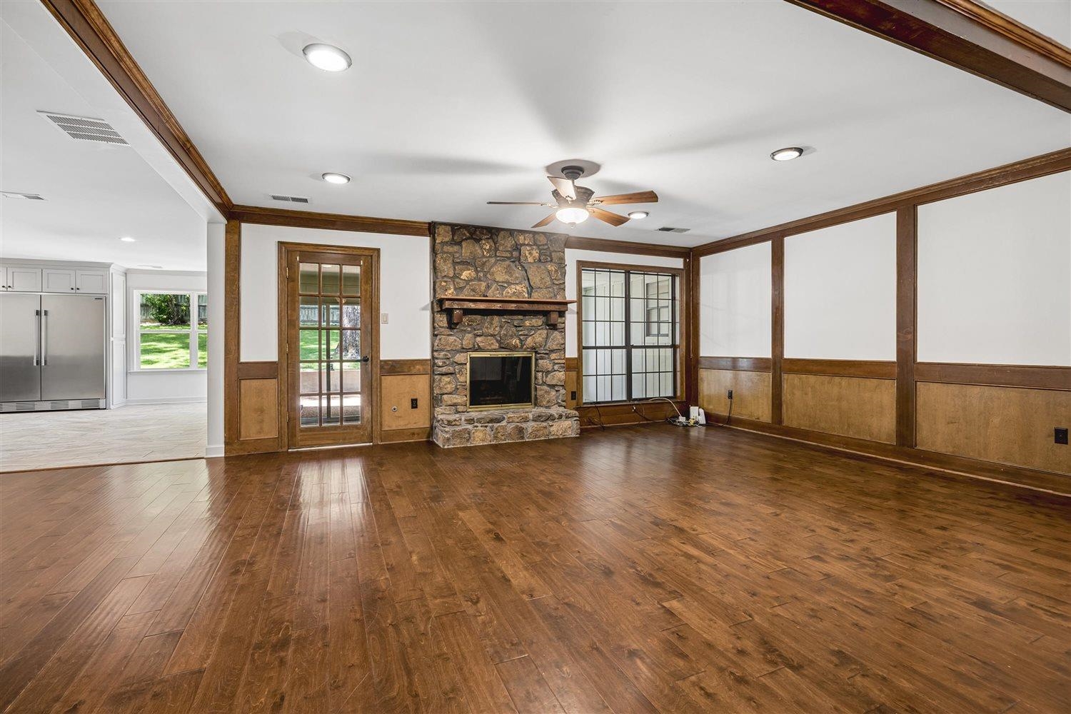 8970 Farmoor Road Germantown, TN 38139 - Photo 6 of 35 Spacious living area featuring wood-finish flooring, a stone-clad fireplace with a wood mantel, a ceiling fan with integrated lighting, recessed ceiling lights, and paneling with contrasting white wall sections