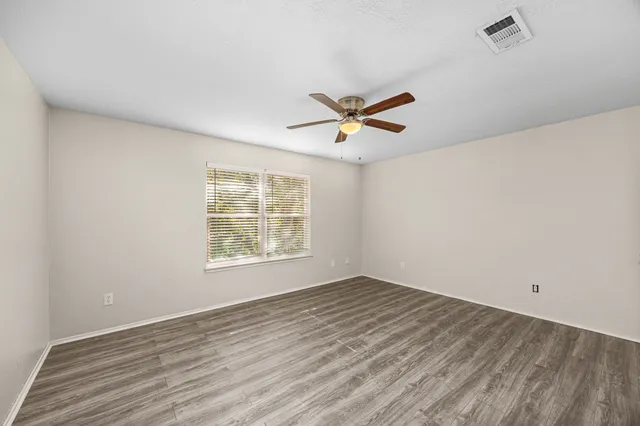 an empty room with wooden floor chandelier fan and windows