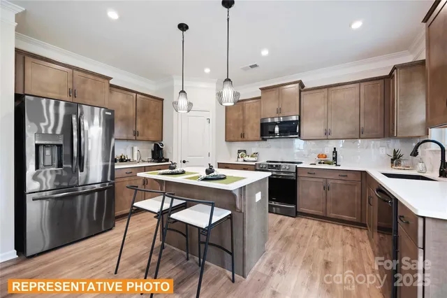 a kitchen with stainless steel appliances a stove a sink a refrigerator a center island and chairs