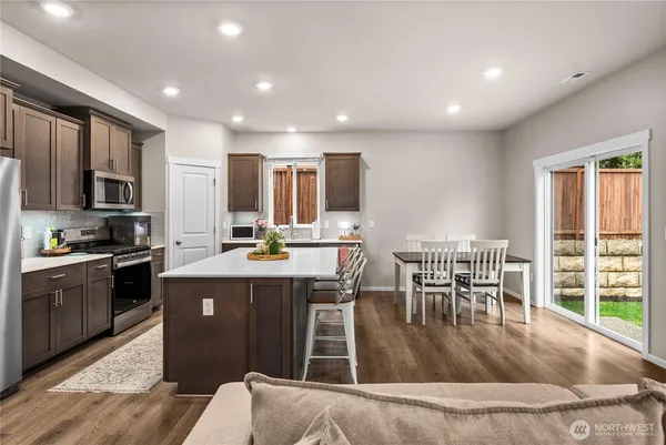 a kitchen with kitchen island granite countertop a stove top oven a sink a dining table and chairs with wooden floor