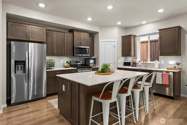 a kitchen with kitchen island granite countertop wooden cabinets a refrigerator a stove a oven with a dining table and chairs