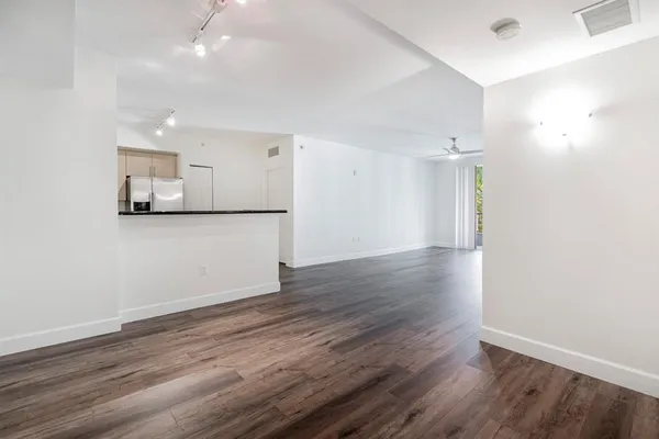 an empty room with wooden floor and kitchen view