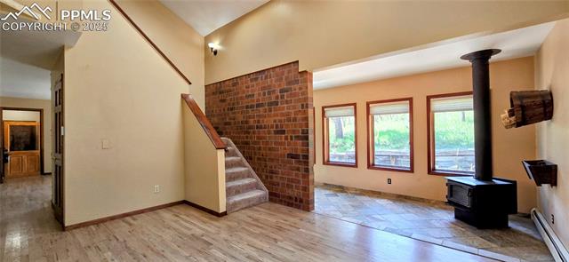 18170 Forest View Road Monument, CO 80132 - Photo 8 of 32 Unfurnished living room featuring a wood stove, baseboard heating, light wood-type flooring, stairs, and baseboards
