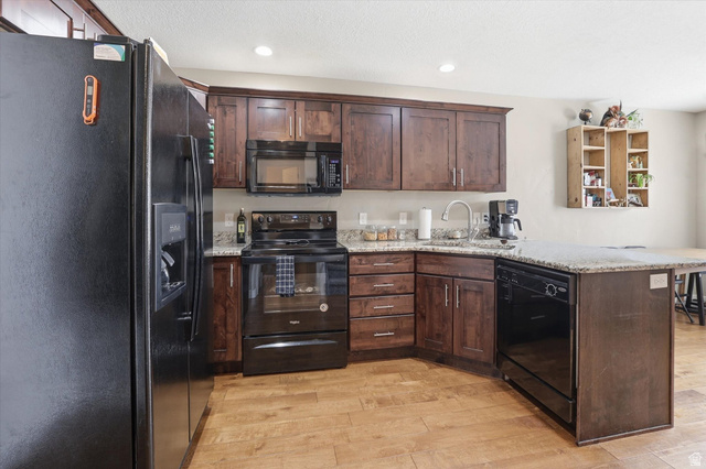 1024 South 270 West Logan, UT 84321 - Photo 10 of 37 Kitchen featuring black appliances, dark wood finish cabinets, a peninsula, light stone counters, and recessed lighting