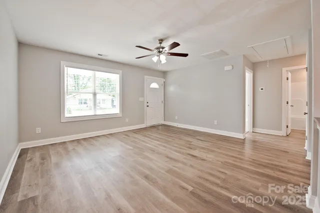 an empty room with wooden floor ceiling fan and windows