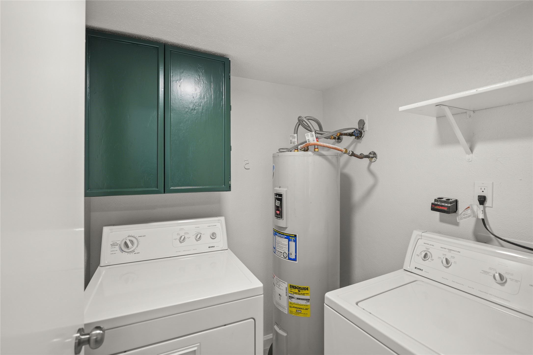 6610 Blue Ridge Drive Richmond, TX 77469 - Photo 19 of 24 This photo shows the laundry room equipped with a washer and dryer, a water heater, green storage cabinets, and a wall shelf for additional storage.