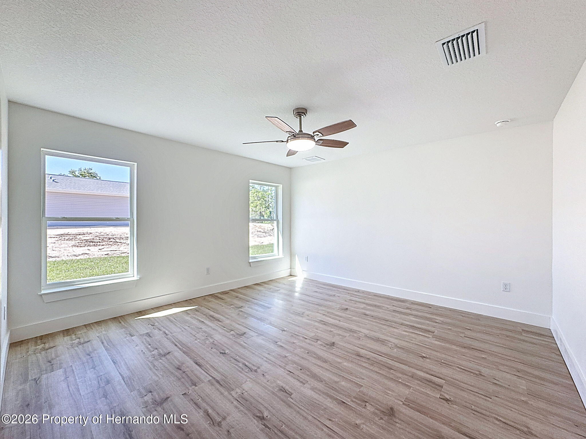 8988 Waterbird Way Weeki Wachee, FL 34613 - Photo 22 of 42 an empty room with wooden floor chandelier fan and windows