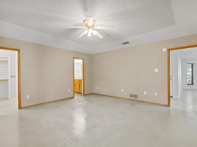 an empty room with chandelier fan and windows