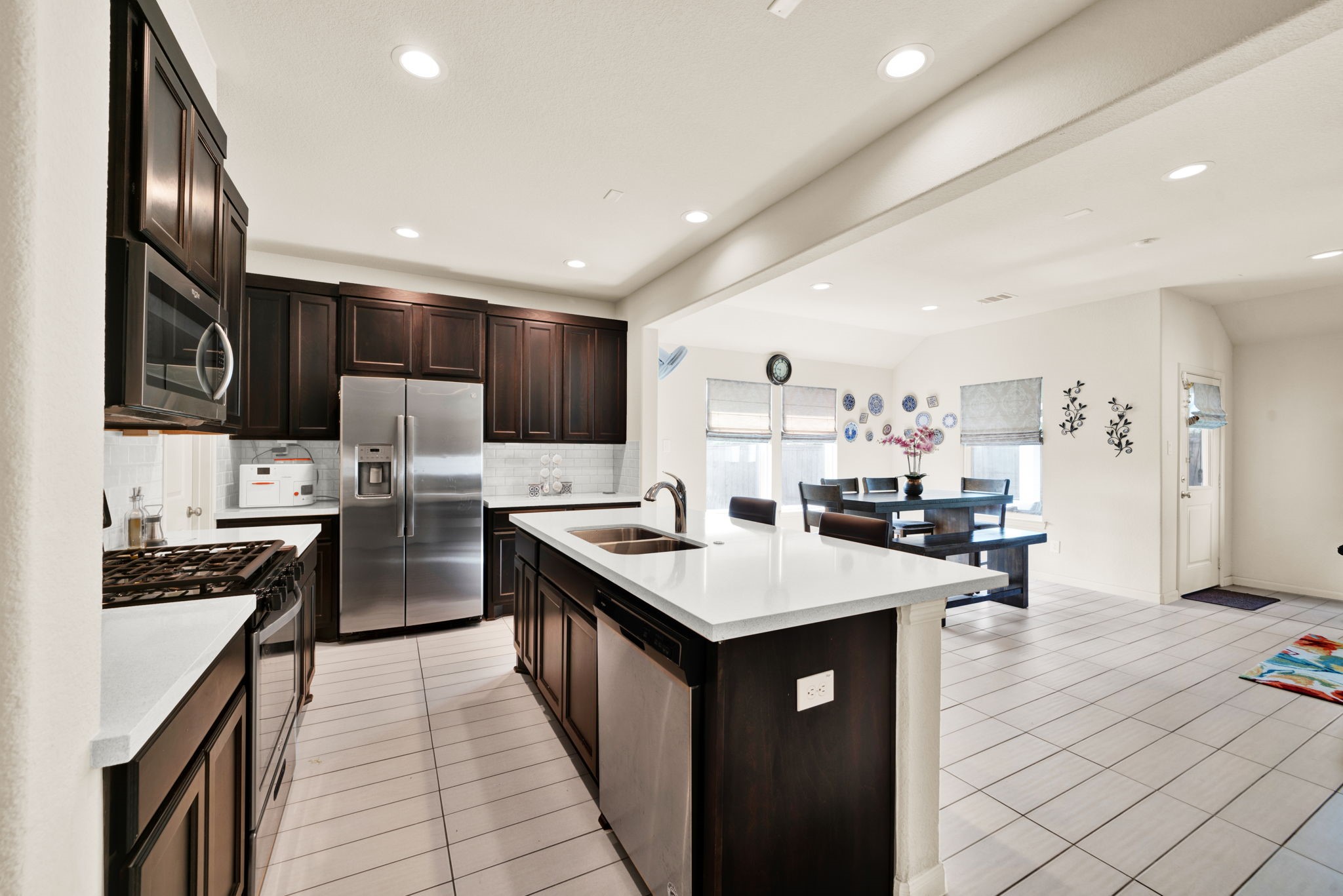 2503 Hagerman Road Conroe, TX 77384 - Photo 8 of 43 This photo showcases a modern kitchen with dark wood cabinets, stainless steel appliances, and a spacious island. It opens to a bright dining area with large windows, offering a clean and contemporary feel.