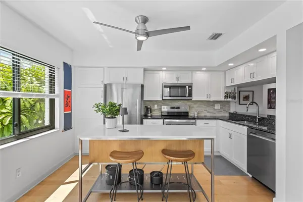a kitchen with stainless steel appliances granite countertop a stove top oven a refrigerator a sink and white cabinets