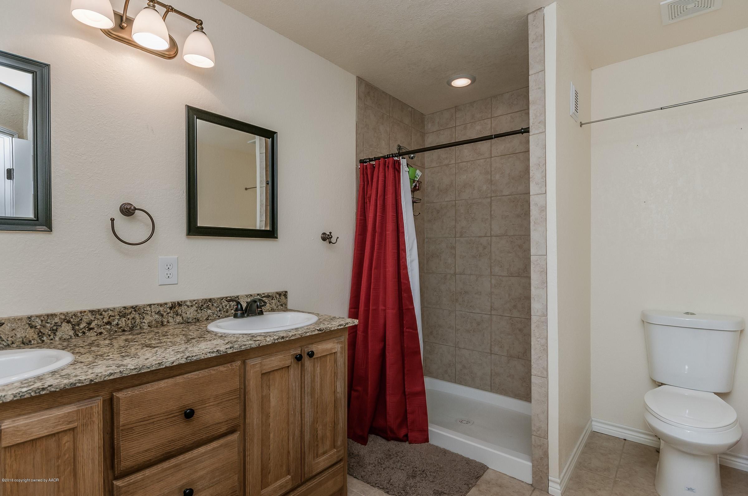 4402 Parker Street Amarillo, TX 79110 - Photo 15 of 21 a bathroom with a granite countertop sink a toilet a mirror and shower