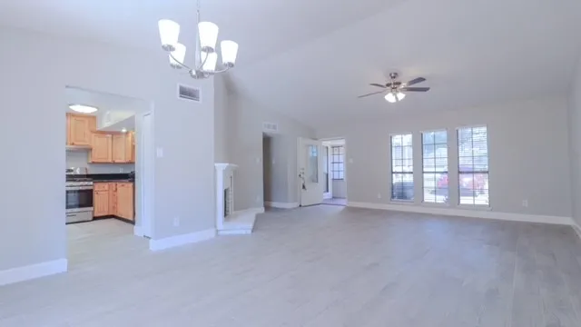a view of an empty room with a chandelier fan and kitchen view