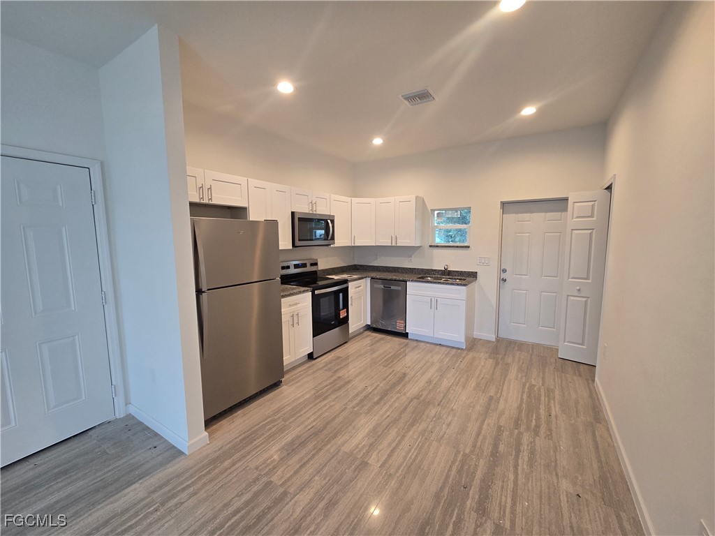 2822 19th Street Southwest Lehigh Acres, FL 33976 - Photo 7 of 23 a kitchen with wooden floors stainless steel appliances and white cabinets