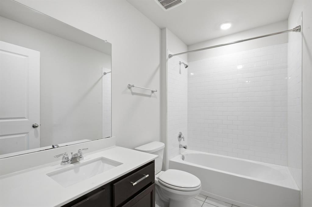 1328 Broaddus Road Forney, TX 75126 - Photo 28 of 31 Full bathroom featuring a dark wood-finish vanity with a white countertop and undermount sink, a large frameless mirror, and a white subway tile surround for the tub and shower combination