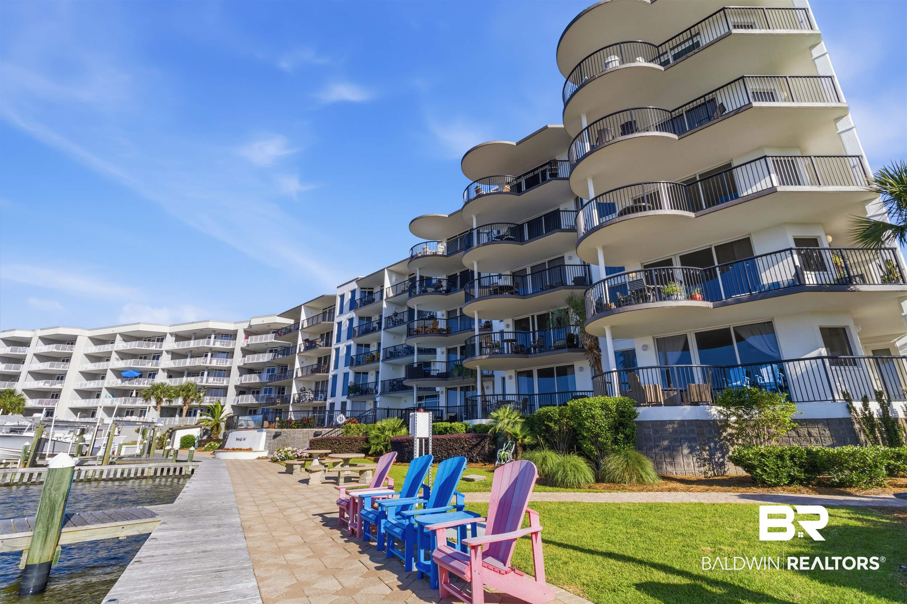 3564 Bayou Road, Unit 203 Orange Beach, AL 36561 - Photo 41 of 53 Multi-story condominium building featuring expansive balconies with black railings, a paved patio area, and a waterfront pier