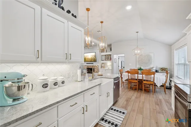 a very nice looking kitchen with granite countertop a stove a sink a dining table and chairs with wooden floor