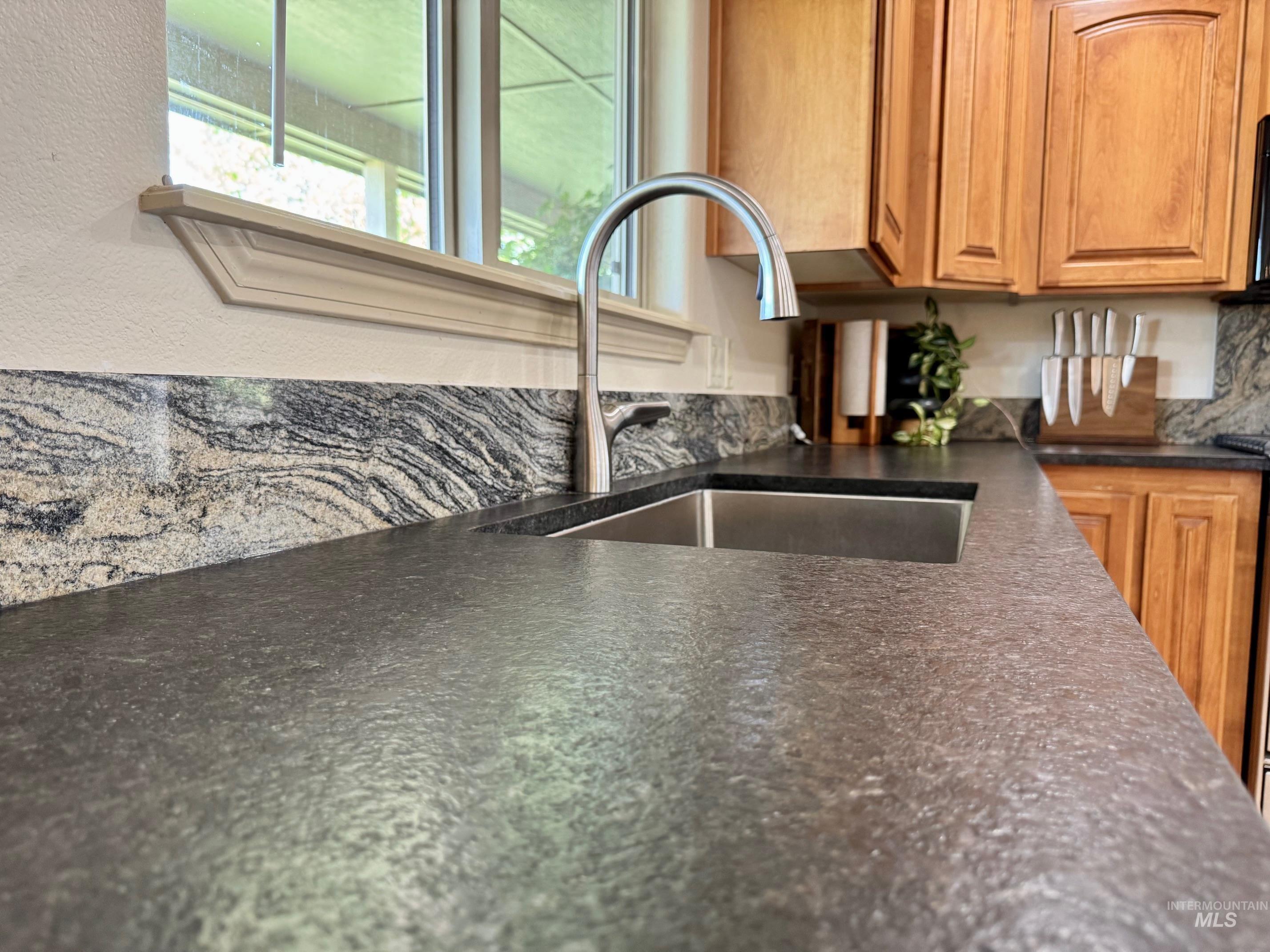 9299 Kemp Road Middleton, ID 83644 - Photo 14 of 50 Kitchen featuring a stainless steel undermount sink with a gooseneck faucet, dark textured countertops, and a patterned stone backsplash