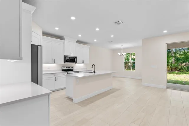 a large white kitchen with stainless steel appliances granite countertop a stove a sink a refrigerator and a cabinets