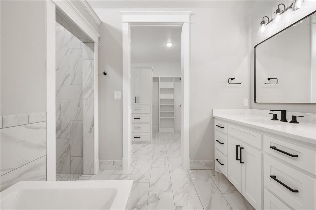 6610 Waggoner Way Midlothian, TX 76065 - Photo 23 of 40 Spacious bathroom featuring a double vanity with white cabinetry and black hardware, a large rectangular mirror with black frame, and a tub with marble-look tile surround