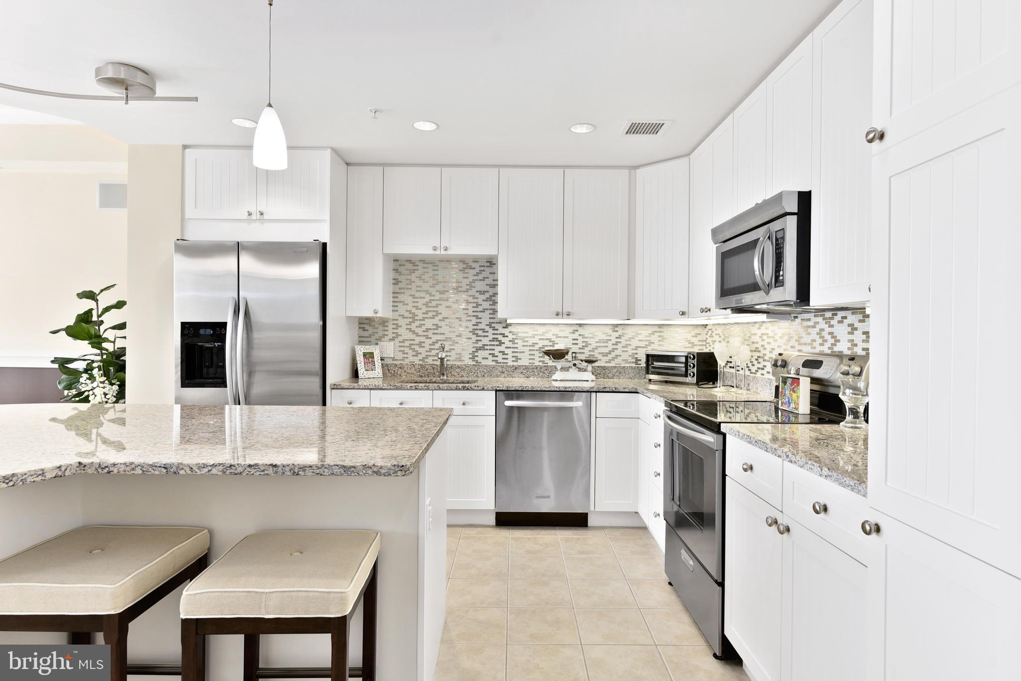 a kitchen with stainless steel appliances granite countertop a stove top oven a refrigerator a sink and white cabinets