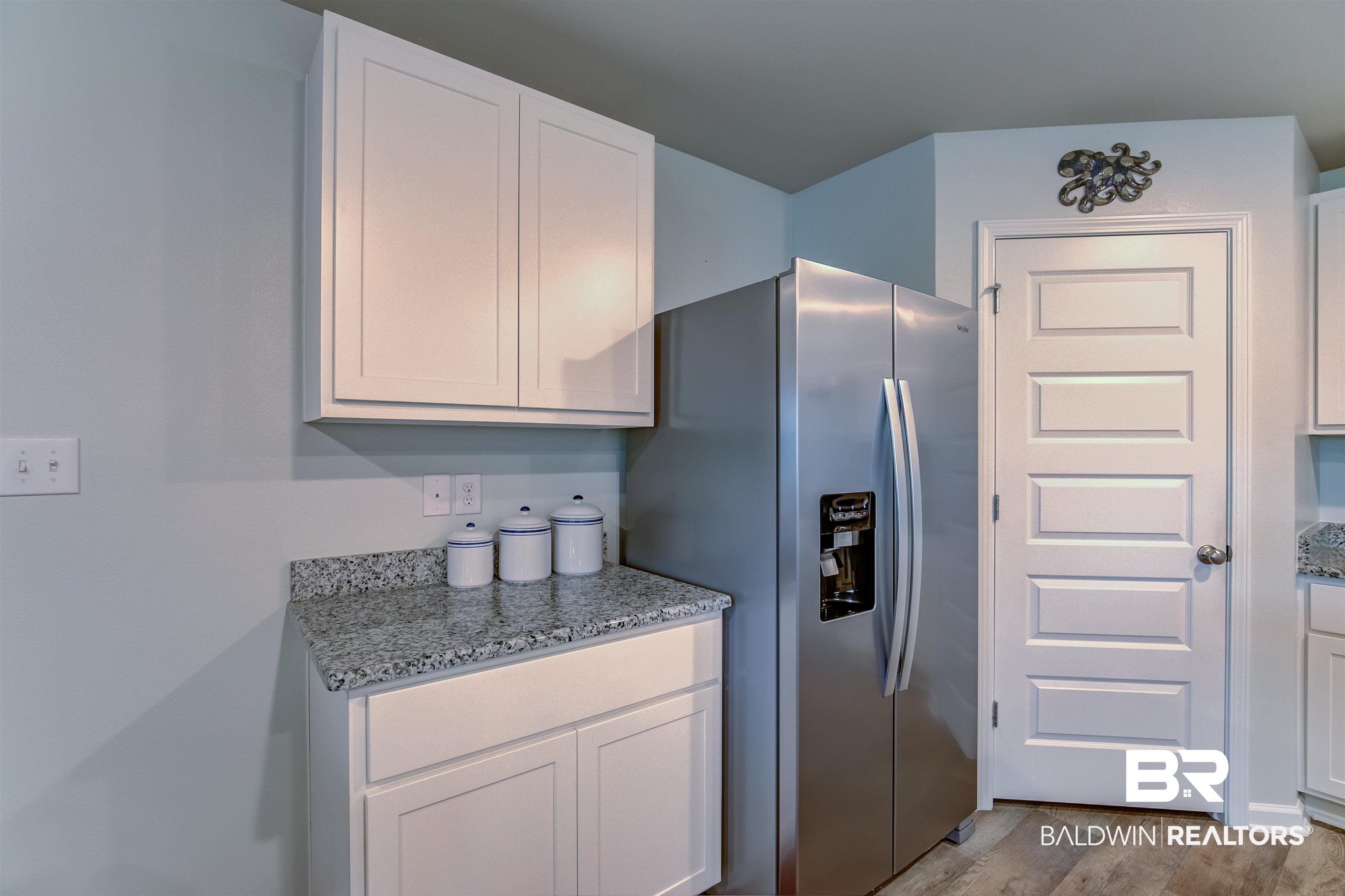 8033 Irwin Loop Daphne, AL 36526 - Photo 16 of 38 Kitchen area featuring light cabinetry, a speckled countertop, stainless steel refrigerator, and wood-finish flooring