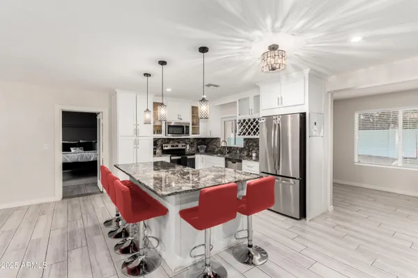 a kitchen with stainless steel appliances kitchen island granite countertop a refrigerator a stove top oven a dining table and chairs with wooden floor