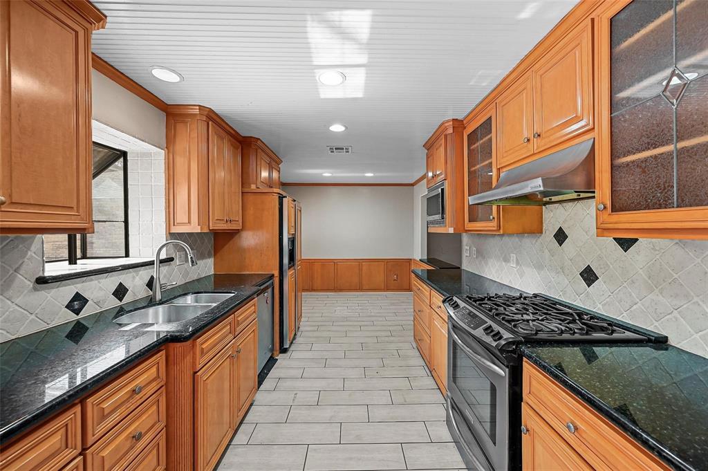 412 West Spinner Road DeSoto, TX 75115 - Photo 5 of 13 Galley kitchen featuring wood cabinetry, dark countertops, stainless steel appliances, tiled backsplash, and recessed lighting