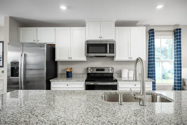 a kitchen with stainless steel appliances granite countertop a stove a sink a microwave a refrigerator and white cabinets with wooden floor