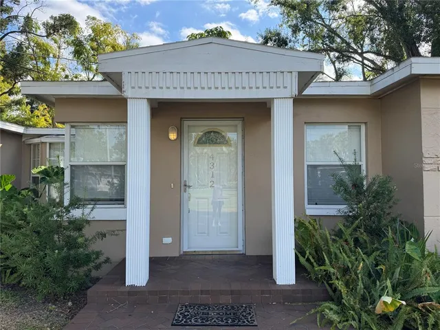 a view of a brick house with plants and large tree