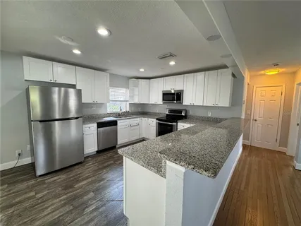 a kitchen with granite countertop a refrigerator a sink dishwasher and a stove with wooden floor