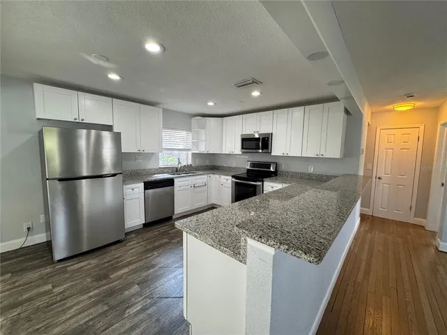 a kitchen with granite countertop a refrigerator a sink dishwasher and a stove with wooden floor