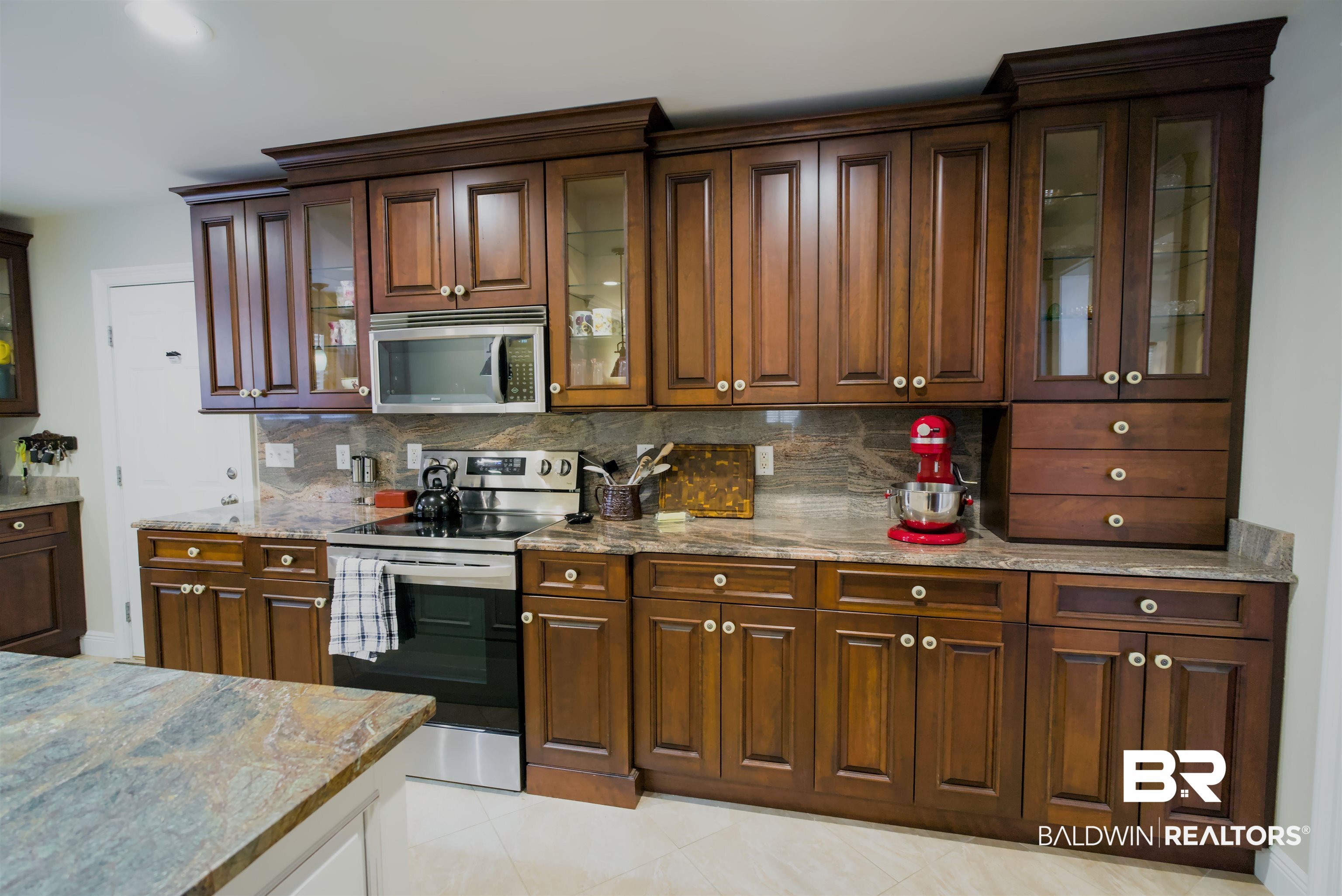 373 Collinwood Loop Foley, AL 36535 - Photo 12 of 49 Kitchen featuring dark wood cabinetry with crown molding, stone countertops, a tiled backsplash, and stainless steel appliances including a built-in microwave and range