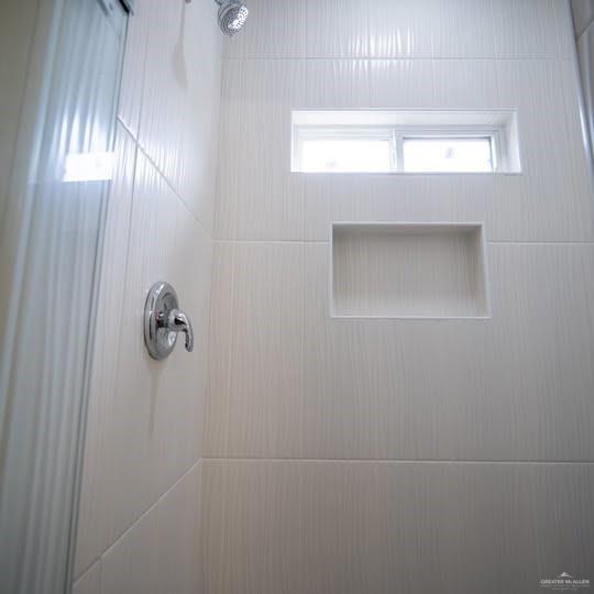 3052 Briggs Road, Unit C Weslaco, TX 78596 - Photo 14 of 16 Shower enclosure featuring textured light-colored tile walls, a built-in shower niche, a recessed window, a chrome shower head, and a chrome single-handle control