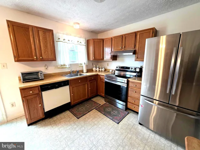 a kitchen with granite countertop stainless steel appliances a sink a stove a refrigerator a window and cabinets