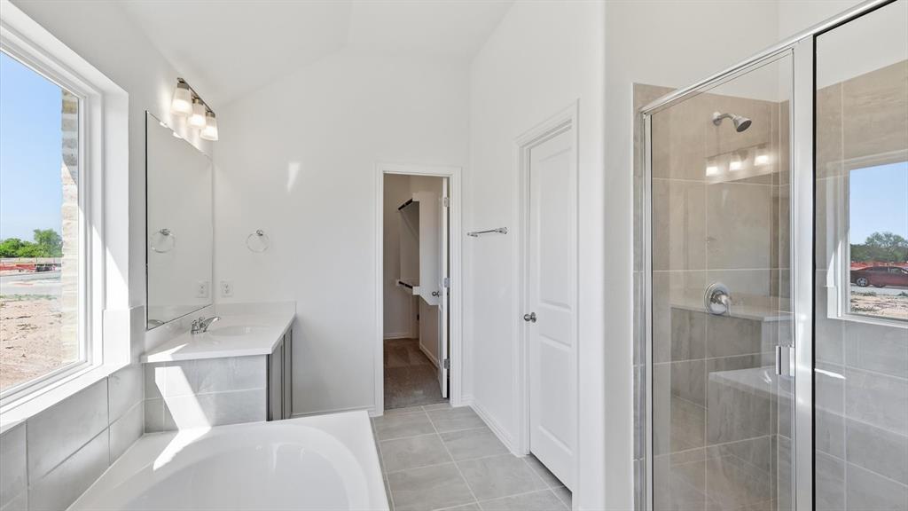 2529 Rivers W Road Anna, TX 75409 - Photo 31 of 40 Bright bathroom featuring a glass-enclosed shower with integrated bench seating, a separate soaking tub, a single vanity with an undermount sink and stone-finish countertop, and tiled flooring
