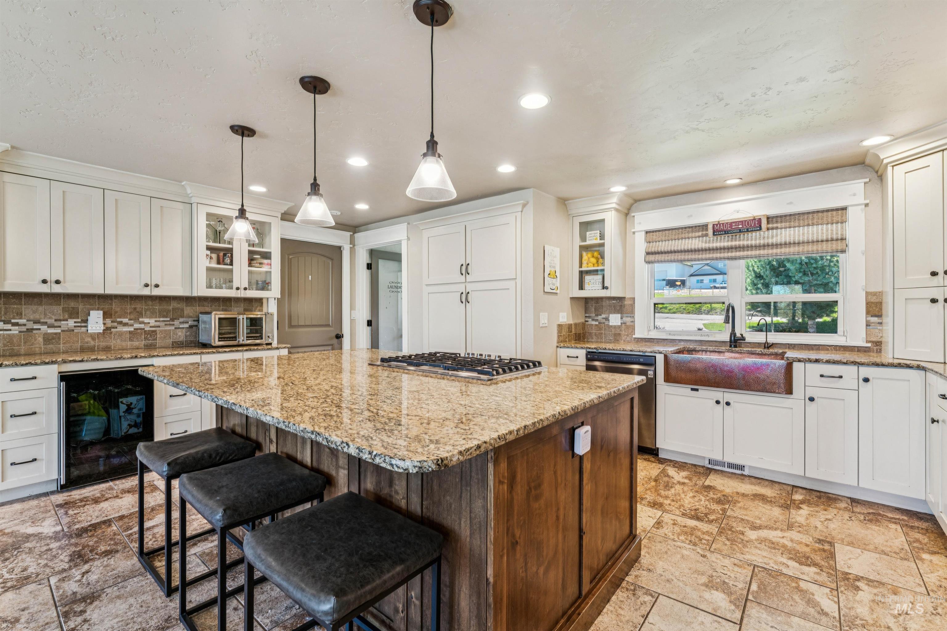 1050 West South Slope Road Emmett, ID 83617 - Photo 11 of 49 Kitchen featuring glass insert cabinets, tasteful backsplash, a center island, a kitchen bar, and light stone counters
